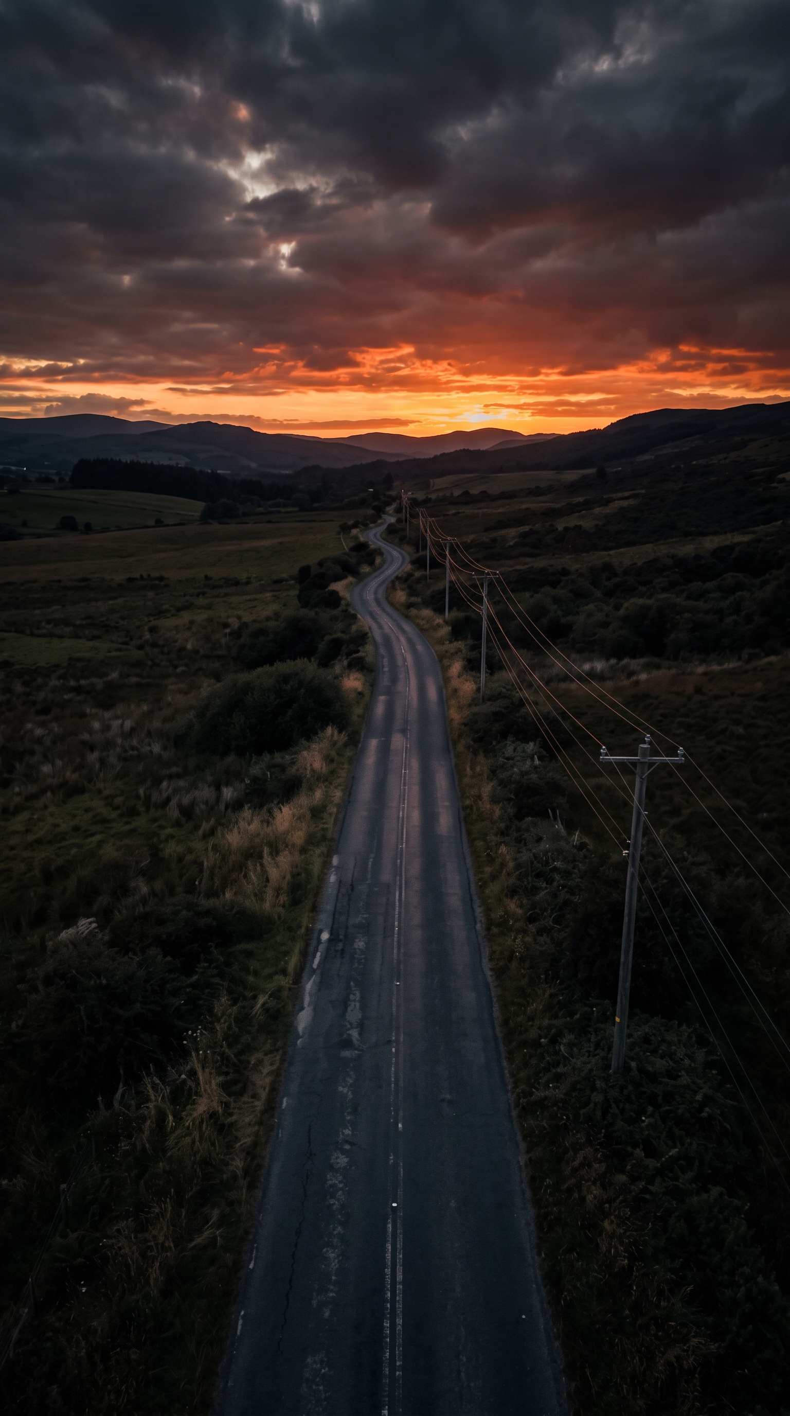Photorealistic photo of empty road at sunset with power lines, high-angle view from above, moody dark tones, dramatic lighting, 9:16 aspect ratio
