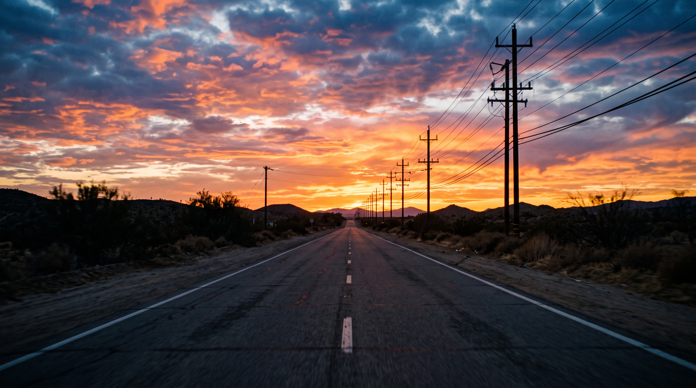 Cinematic film still of empty road at sunset with power lines, centered subject with a simple uncluttered composition, vivid colors, high contrast, energetic, 16:9 aspect ratio