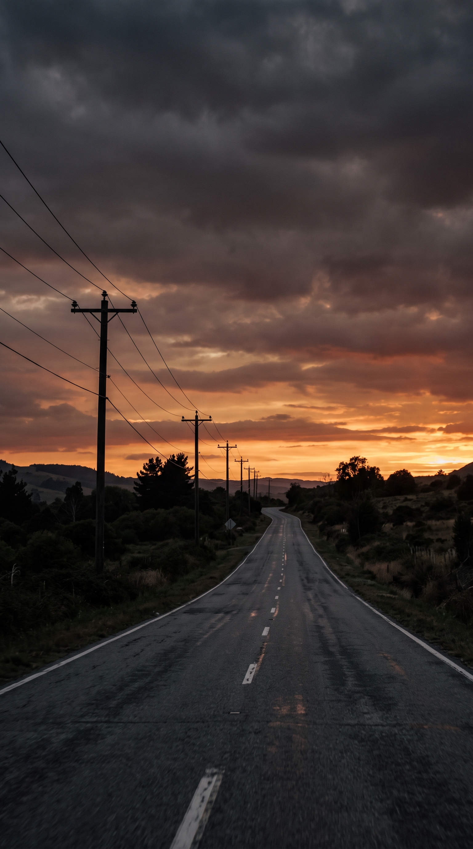 Cinematic film still of empty road at sunset with power lines, wide shot with open space at the top for text, moody dark tones, dramatic lighting, 9:16 aspect ratio