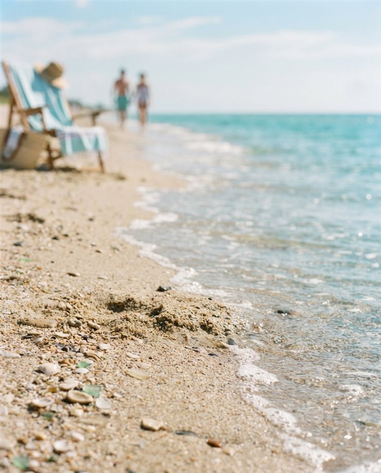 Cinematic film still of sandy beach with clear turquoise water, close-up detail with shallow depth of field, soft pastel colors, bright and cozy, 4:5 aspect ratio
