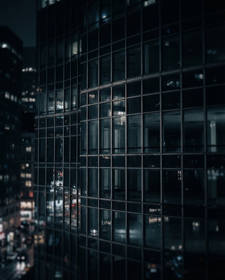 Cinematic film still of modern glass building, close-up detail with shallow depth of field, moody dark tones, dramatic lighting, 4:5 aspect ratio