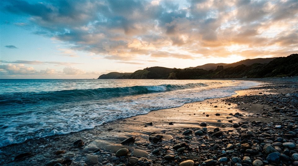 Cinematic film still of a calm wave touching a quiet pebble shore, wide shot with open space at the top for text, vivid colors, high contrast, energetic, 16:9 aspect ratio