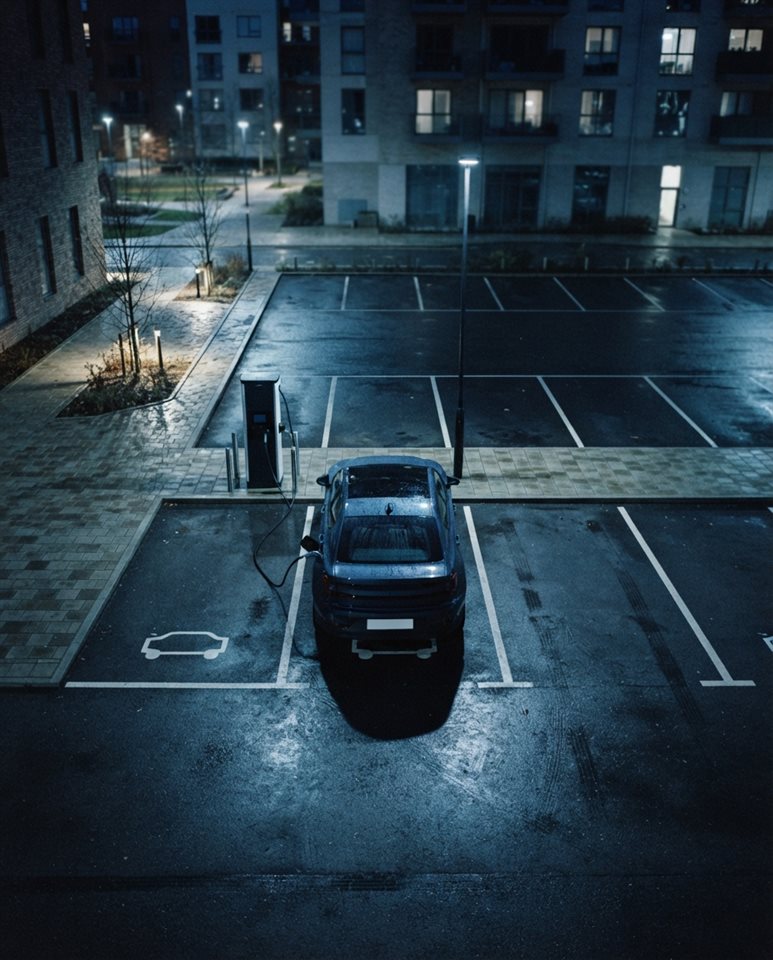 Cinematic film still of an electric car charging at a station, high-angle view from above, cool blue tones, quiet atmosphere, 4:5 aspect ratio