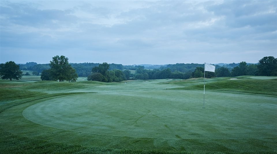 Photorealistic photo of a golf course green with a flag, wide shot with open space at the top for text, cool blue tones, quiet atmosphere, 16:9 aspect ratio