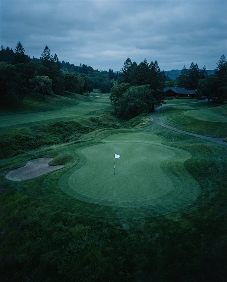 Cinematic film still of a golf course green with a flag, high-angle view from above, cool blue tones, quiet atmosphere, 4:5 aspect ratio