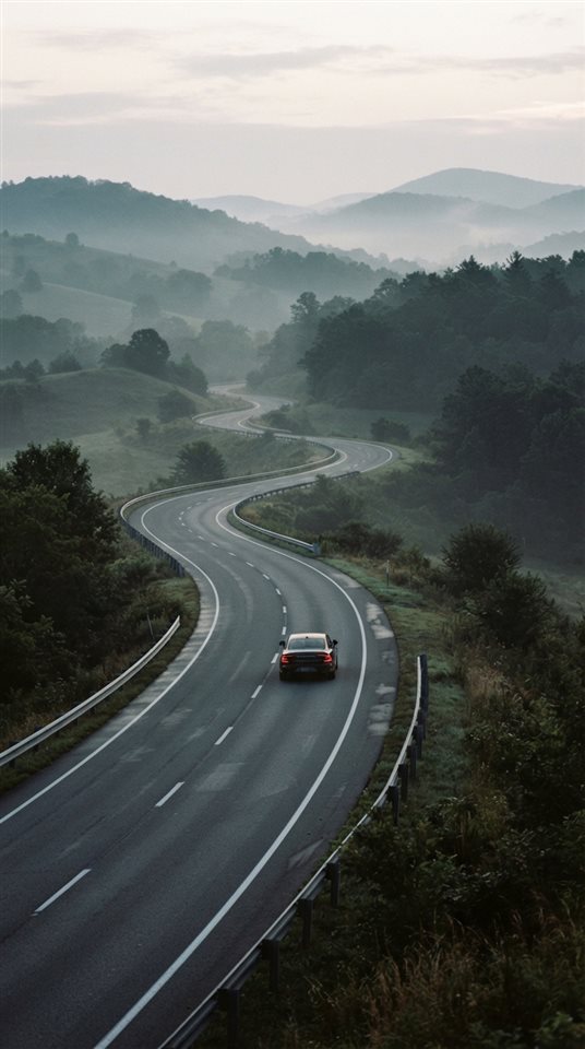 Cinematic film still of a highway winding through hills, centered subject with a simple uncluttered composition, misty morning haze, dreamy, 9:16 aspect ratio
