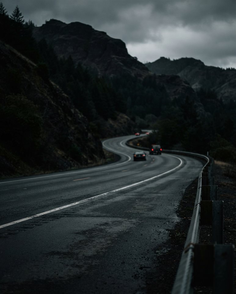 Cinematic film still of a highway winding through hills, close-up detail with shallow depth of field, moody dark tones, dramatic lighting, 4:5 aspect ratio