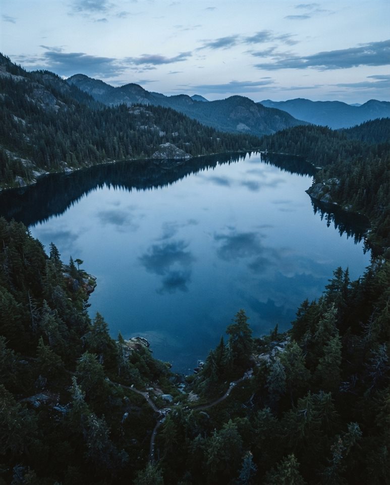 Cinematic film still of calm lake reflecting the sky, high-angle view from above, cool blue tones, quiet atmosphere, 4:5 aspect ratio