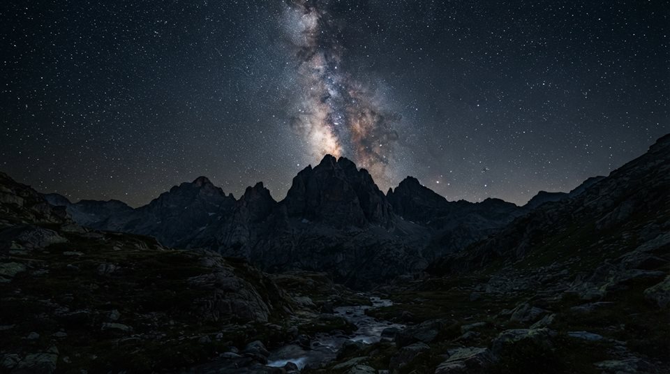 Photorealistic photo of milky way over mountains, centered subject with a simple uncluttered composition, moody dark tones, dramatic lighting, 16:9 aspect ratio