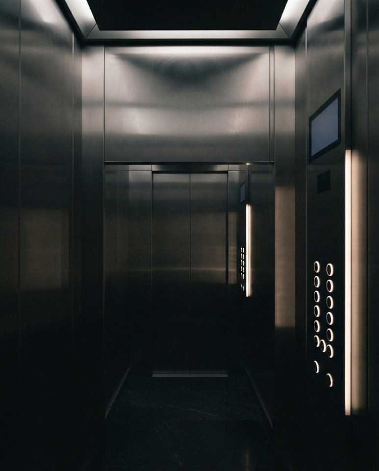 Photorealistic photo of interior of a modern sleek stainless steel elevator with illuminated buttons, wide shot with open space at the top for text, moody dark tones, dramatic lighting, 4:5 aspect ratio