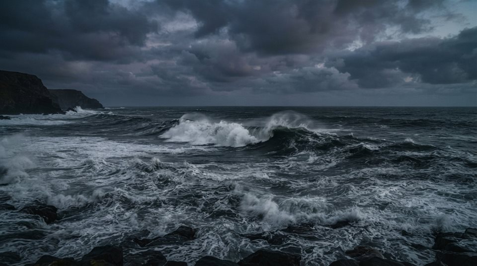 Photorealistic photo of ocean waves, wide shot with open space at the top for text, moody dark tones, dramatic lighting, 16:9 aspect ratio