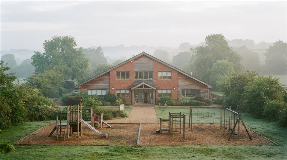 Photorealistic photo of a school building with a playground, centered subject with a simple uncluttered composition, misty morning haze, dreamy, 16:9 aspect ratio