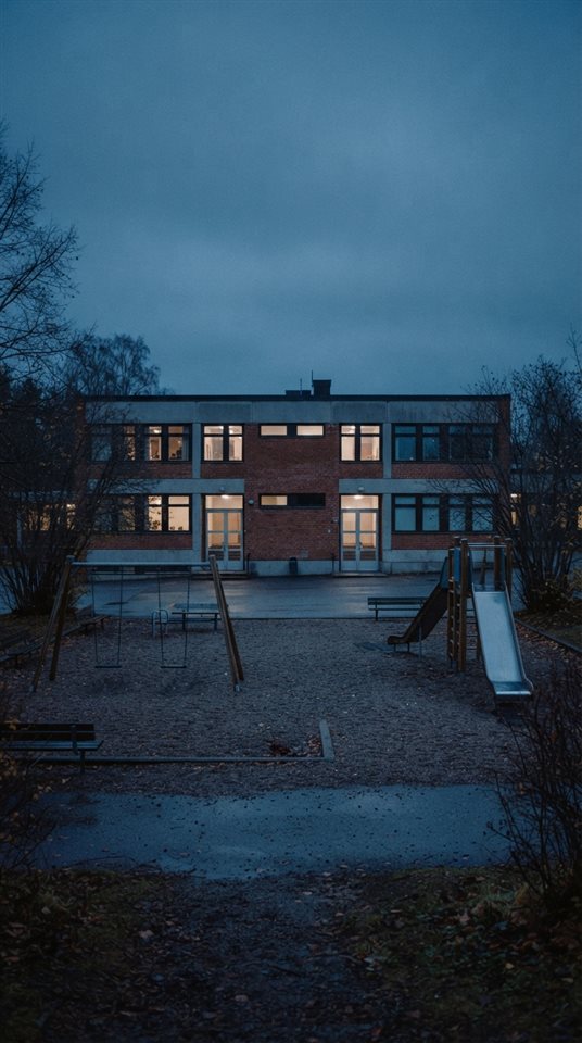 Cinematic film still of a school building with a playground, centered subject with a simple uncluttered composition, cool blue tones, quiet atmosphere, 9:16 aspect ratio