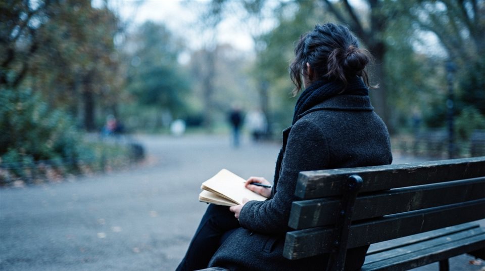 Photorealistic photo of person sitting alone on a park bench seen from behind, close-up detail with shallow depth of field, cool blue tones, quiet atmosphere, 16:9 aspect ratio