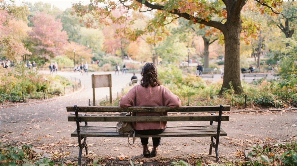 Cinematic film still of person sitting alone on a park bench seen from behind, high-angle view from above, soft pastel colors, bright and cozy, 16:9 aspect ratio