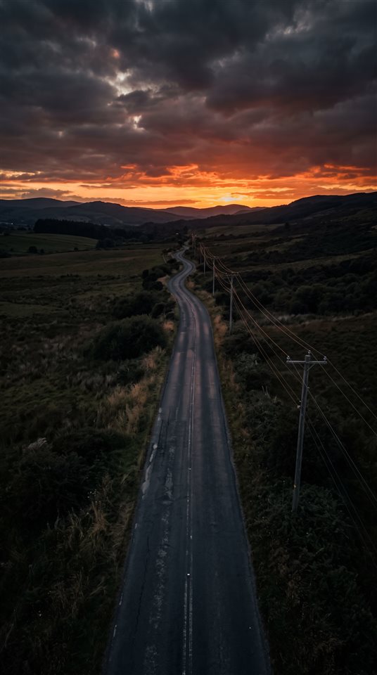Foto fotorrealista de uma estrada vazia ao pôr do sol com postes de energia, visão de alto ângulo de cima, tons escuros e melancólicos, iluminação dramática, proporção 9:16