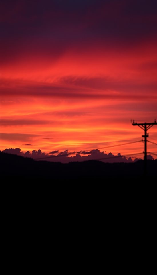 Photorealistic photo of A vibrant evening horizon with brilliant gradients of orange, pink, and purple clouds over a calm silhouette landscape., close-up detail with shallow depth of field, moody dark tones, dramatic lighting, 9:16 aspect ratio