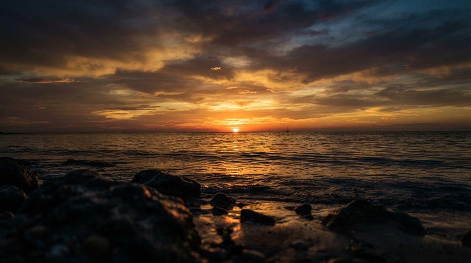 Photorealistic photo of Realistic photo of a golden sunset over a calm ocean viewed from eye level, with empty sky space on top for text, horizontal landscape format, close-up detail with shallow depth of field, moody dark tones, dramatic lighting, 16:9 aspect ratio