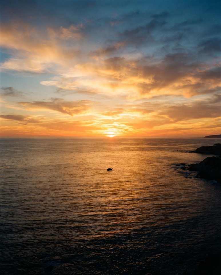 Cinematic film still of Realistic photo of a golden sunset over a calm ocean viewed from eye level, with empty sky space on top for text, horizontal landscape format, high-angle view from above, vivid colors, high contrast, energetic, 4:5 aspect ratio