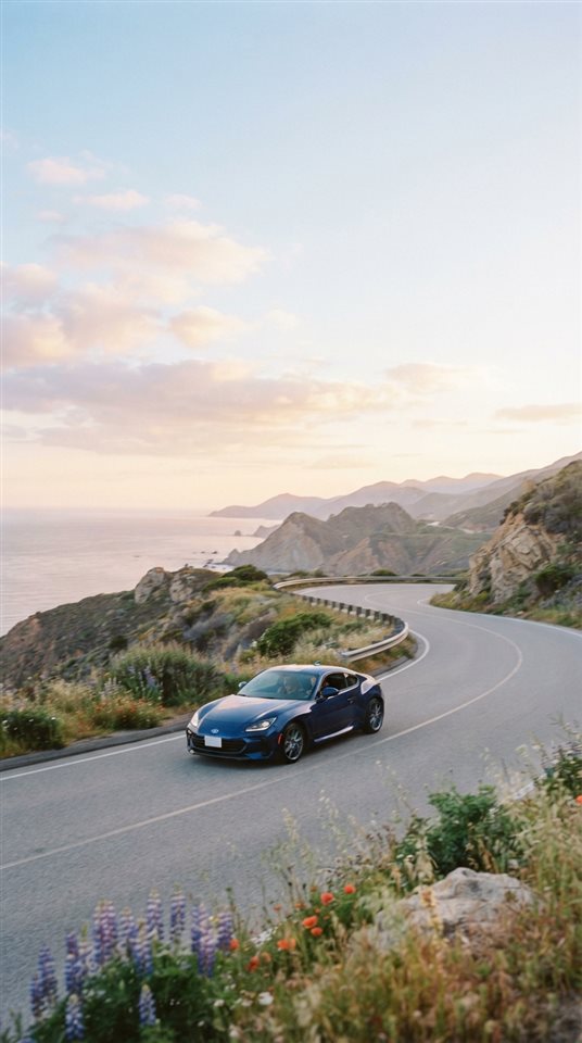 Cinematic film still of sleek generic sports car on an empty road, no brand badges, wide shot with open space at the top for text, soft pastel colors, bright and cozy, 9:16 aspect ratio