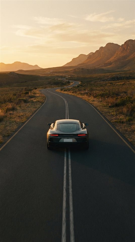 Cinematic film still of sleek generic sports car on an empty road, no brand badges, centered subject with a simple uncluttered composition, warm golden light, calm mood, 9:16 aspect ratio
