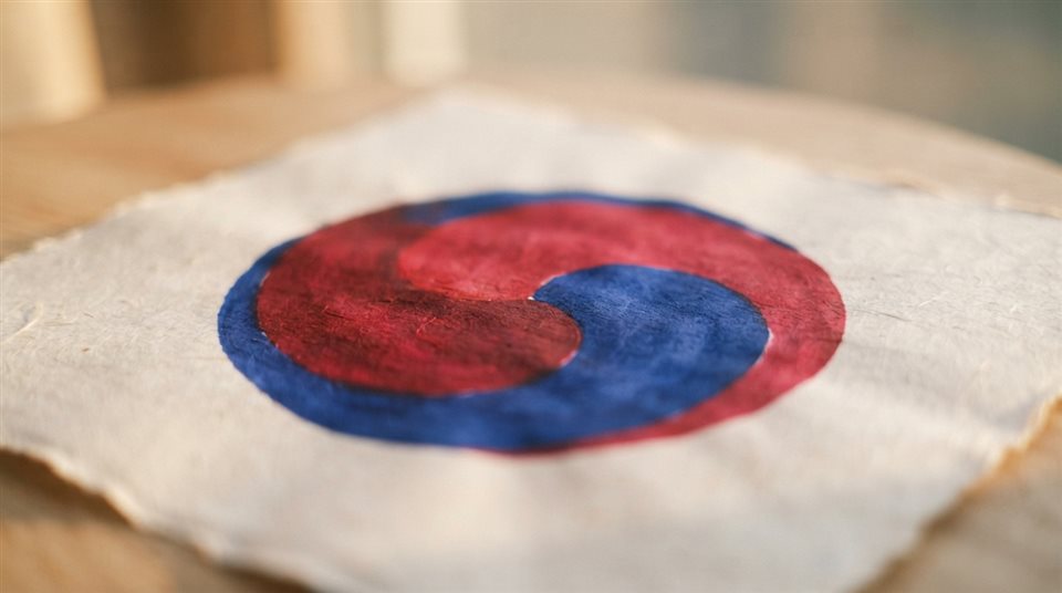 Photorealistic photo of an abstract red and blue taegeuk swirl design on a clean background, close-up detail with shallow depth of field, warm golden light, calm mood, 16:9 aspect ratio