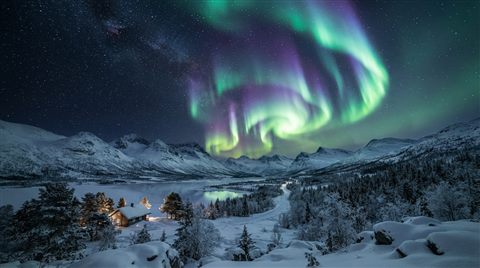 Photorealistic photo of aurora borealis over a snowy landscape, wide shot with open space at the top for text, vivid colors, high contrast, energetic, 16:9 aspect ratio