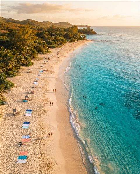 Cinematic film still of sandy beach with clear turquoise water, high-angle view from above, warm golden light, calm mood, 4:5 aspect ratio