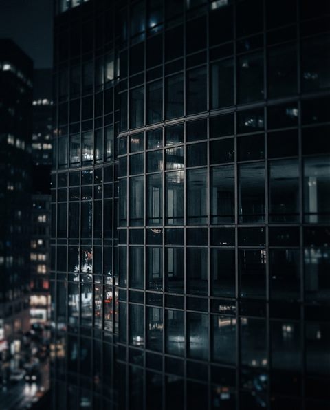 Cinematic film still of modern glass building, close-up detail with shallow depth of field, moody dark tones, dramatic lighting, 4:5 aspect ratio