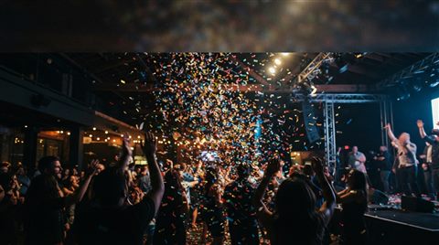 Photorealistic photo of colorful confetti falling, wide shot with open space at the top for text, moody dark tones, dramatic lighting, 16:9 aspect ratio