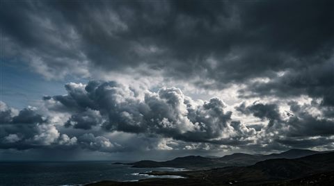Photorealistic photo of fluffy white clouds, wide shot with open space at the top for text, moody dark tones, dramatic lighting, 16:9 aspect ratio