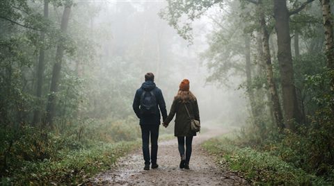Photorealistic photo of a young fictional couple walking together seen from behind, wide shot with open space at the top for text, misty morning haze, dreamy, 16:9 aspect ratio