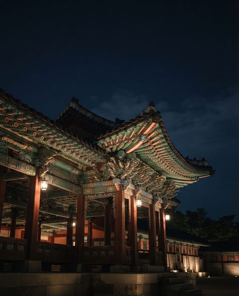 Photorealistic photo of a seamless traditional Korean dancheong pattern in red, green and blue, wide shot with open space at the top for text, moody dark tones, dramatic lighting, 4:5 aspect ratio
