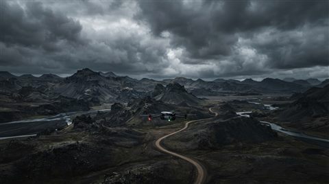 Photorealistic photo of a drone flying over a landscape, wide shot with open space at the top for text, moody dark tones, dramatic lighting, 16:9 aspect ratio