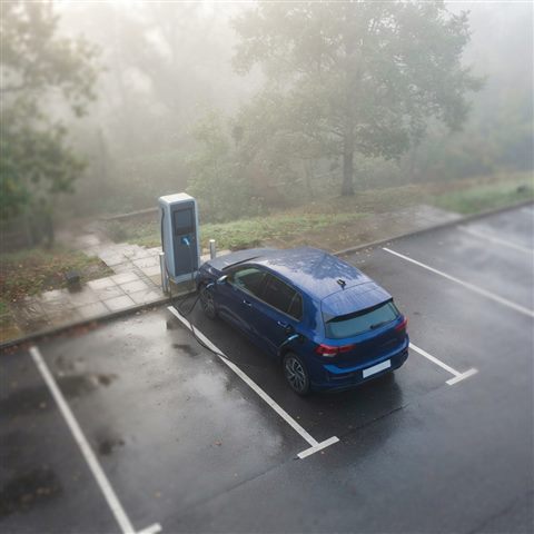 Photorealistic photo of an electric car charging at a station, high-angle view from above, misty morning haze, dreamy, 1:1 aspect ratio