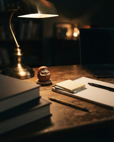 Photorealistic photo of a desk with a lucky charm, sticky notes and warm light for exam day, close-up detail with shallow depth of field, moody dark tones, dramatic lighting, 4:5 aspect ratio