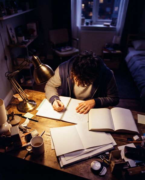 Cinematic film still of a student studying late at night under a desk lamp, high-angle view from above, vivid colors, high contrast, energetic, 4:5 aspect ratio