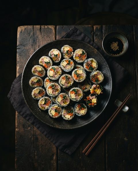 Photorealistic photo of sliced gimbap rolls arranged on a plate, high-angle view from above, moody dark tones, dramatic lighting, 4:5 aspect ratio