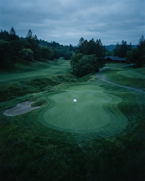 Cinematic film still of a golf course green with a flag, high-angle view from above, cool blue tones, quiet atmosphere, 4:5 aspect ratio