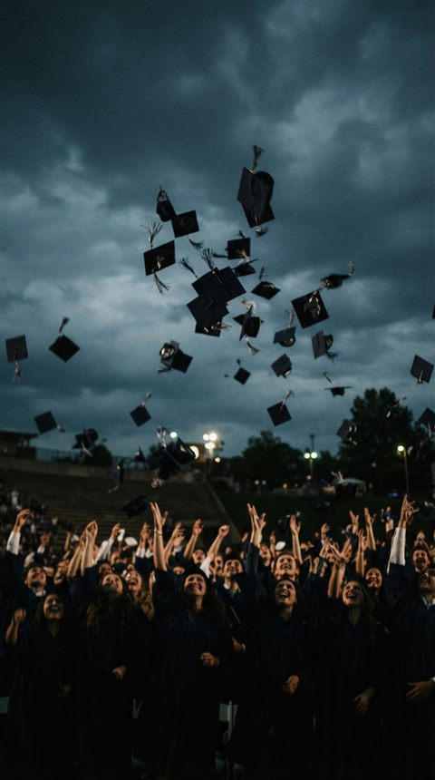 Cinematic film still of graduation caps tossed into the sky, centered subject with a simple uncluttered composition, moody dark tones, dramatic lighting, 9:16 aspect ratio