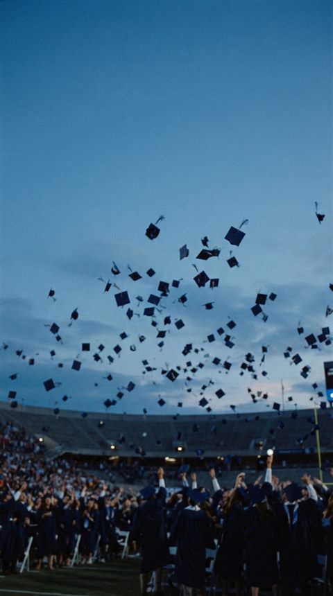 Cinematic film still of graduation caps tossed into the sky, wide shot with open space at the top for text, cool blue tones, quiet atmosphere, 9:16 aspect ratio