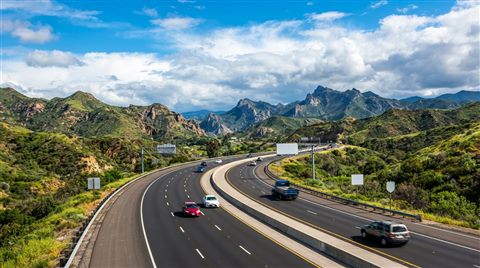 Photorealistic photo of a highway winding through hills, wide shot with open space at the top for text, vivid colors, high contrast, energetic, 16:9 aspect ratio