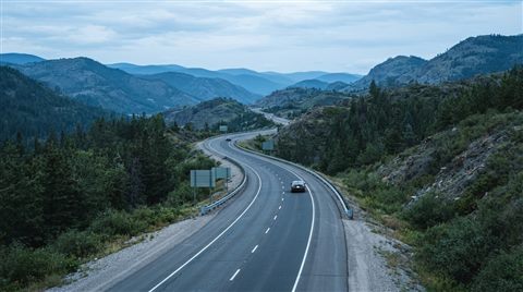 Photorealistic photo of a highway winding through hills, centered subject with a simple uncluttered composition, cool blue tones, quiet atmosphere, 16:9 aspect ratio