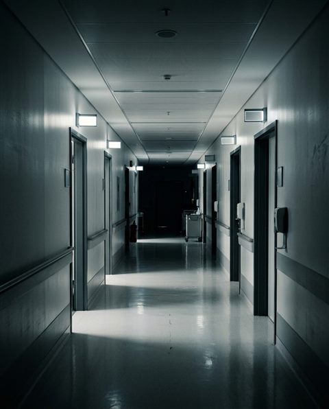 Cinematic film still of a clean modern hospital corridor, high-angle view from above, moody dark tones, dramatic lighting, 4:5 aspect ratio