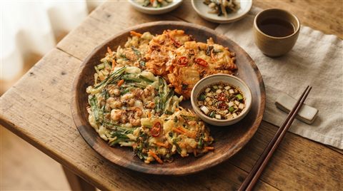 Photorealistic photo of golden Korean pancakes jeon on a wooden plate, high-angle view from above, warm golden light, calm mood, 16:9 aspect ratio