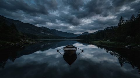 Photorealistic photo of calm lake reflecting the sky, centered subject with a simple uncluttered composition, moody dark tones, dramatic lighting, 16:9 aspect ratio