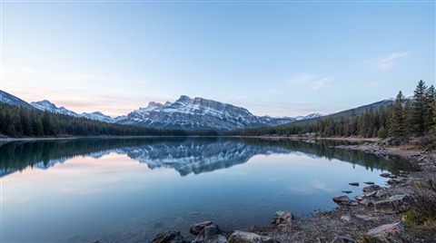 Photorealistic photo of calm lake reflecting the sky, wide shot with open space at the top for text, cool blue tones, quiet atmosphere, 16:9 aspect ratio