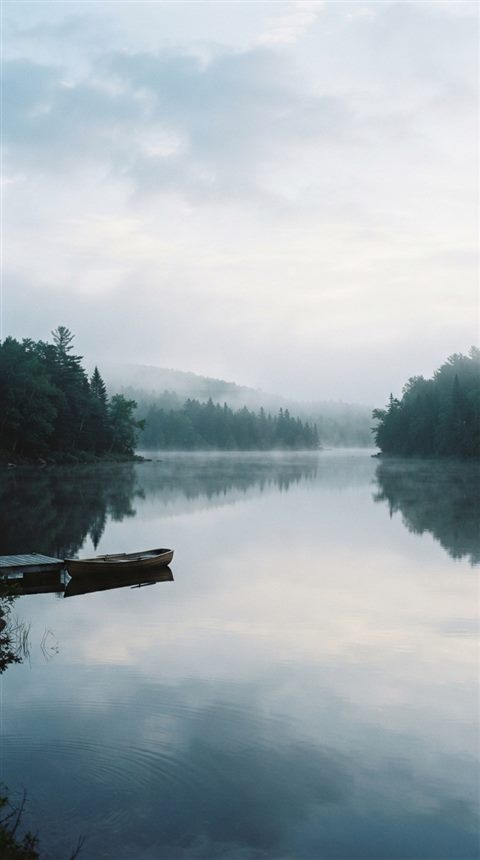 Cinematic film still of calm lake reflecting the sky, wide shot with open space at the top for text, misty morning haze, dreamy, 9:16 aspect ratio