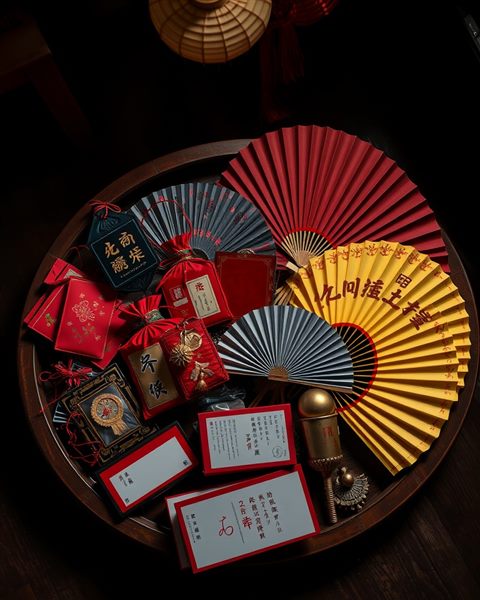 Photorealistic photo of Traditional festive objects including lucky pouches and colorful silk fans arranged neatly on a wooden tray., high-angle view from above, moody dark tones, dramatic lighting, 4:5 aspect ratio