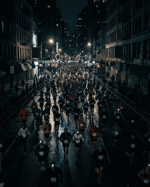 Cinematic film still of runners in a city marathon, high-angle view from above, moody dark tones, dramatic lighting, 4:5 aspect ratio
